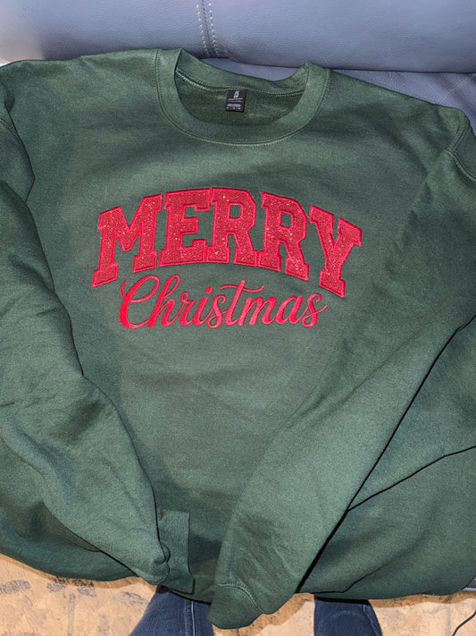 Green sweatshirt with red 'Merry Christmas' text on a light blue surface.