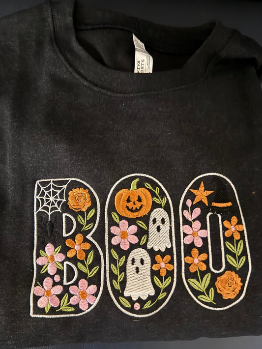 Black sweatshirt with embroidered Halloween design spelling 'BOO' on a dark background